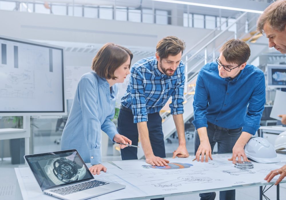 In the Industrial Engineering Facility: Diverse Group of Engineers and Technicians on a Meeting Gather Around Table with Engine Design Technical Drafts, Have Discussion, Analyse Technology